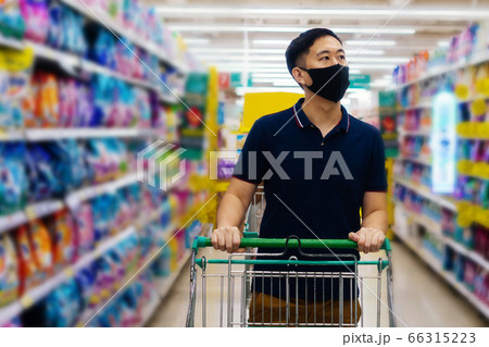 Young adult Asian man wearing a face mask while shopping with cart trolley in grocery supermarket store. 66315223