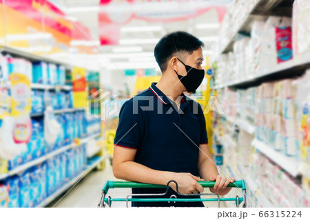 Young adult Asian man wearing a face mask while shopping with cart trolley in grocery supermarket store. 66315224