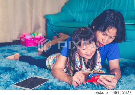 Asian father and daughter little girl watching smart phone lying in living room before ready to sleep in bed room 66315622