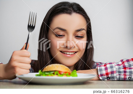 Young pretty woman adheres to diet but chooses unhealthy food Young pretty woman adheres to diet but chooses unhealthy food 66316276