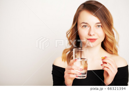Young woman holding a glass of water and a pill for weight loss 66321394