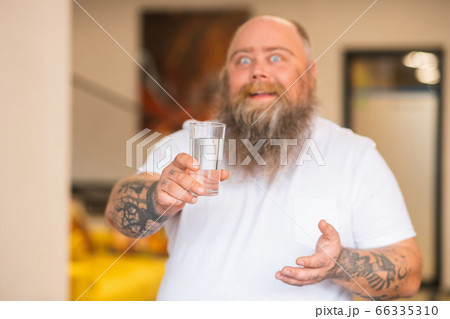 Bald bearded plump man holding a glass of water in his hand Bald bearded plump man holding a glass of water in his hand 66335310
