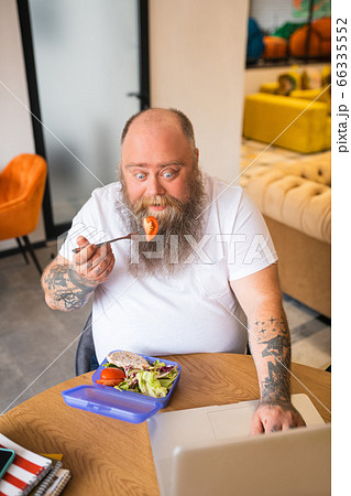 Bald bearded abdominous man in white tshirt having lhis meal Bald bearded abdominous man in white tshirt having lhis meal 66335552