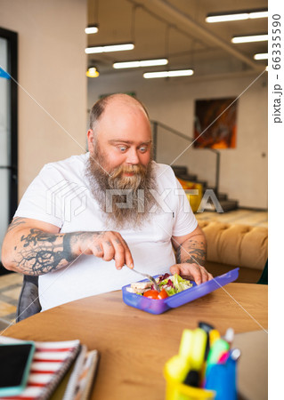 Bald bearded man in white tshirt eating his lunch 66335590