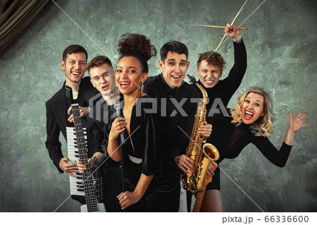 Cheerful international music group on a gray wall background, a group of musicians posing on camera in the hands of various instruments, guitars, saxophone. Copy space. 66336600