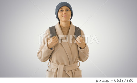 Young woman wearing coat and backpack walking on gradient background. 66337330