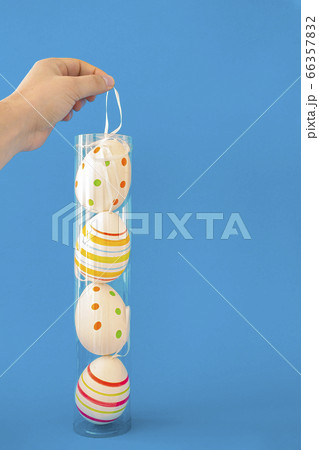 A Person holding a container of colorful Easter eggs with a hanger on a blue background 66357832