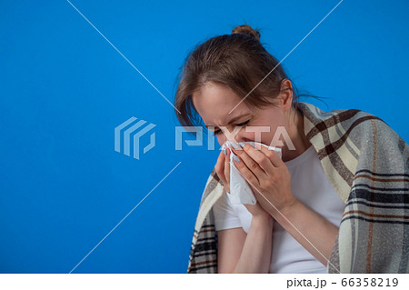 Woman feeling sick, sneezing into facial tissue against blue wall at home 66358219