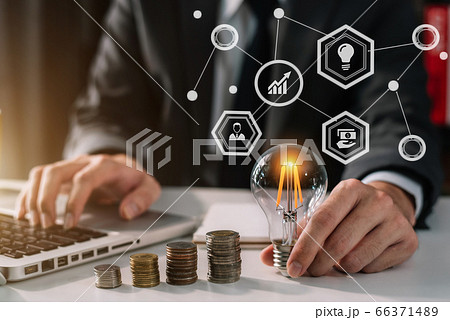 businessman hand holding lightbulb with using laptop computer and money stack in office. idea saving energy and accounting finance concept in office. 66371489