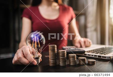 businessman hand holding lightbulb with using laptop computer and money stack in office. idea saving energy and accounting finance concept in office. 66371494