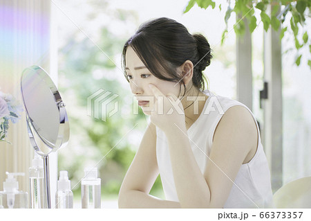 リビングでお肌のお手入れをする若い女性［悩んでいる］ 66373357