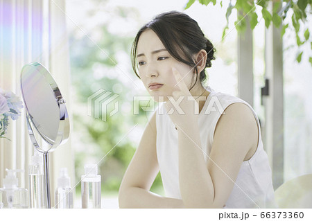 リビングでお肌のお手入れをする若い女性［悩んでいる］ 66373360