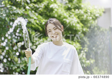 庭にホースで水をまく若い女性 夏のイメージ の写真素材