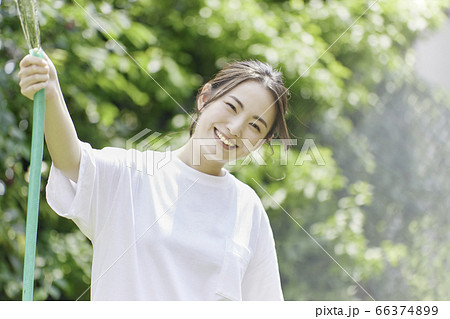 庭にホースで水をまく若い女性 夏のイメージ の写真素材