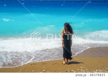 Happy woman traveler stands on the shore in a coming wave and the wind plays in her hair 66376835
