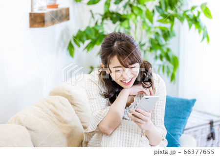 リビングのソファでスマホを見ながら微笑む女性 リビングのソファでスマホを見ながら微笑む女性 66377655