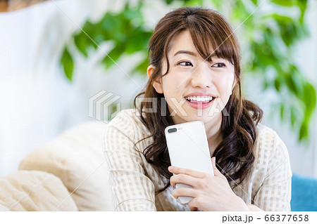 リビングのソファでスマホを見ながら微笑む女性 66377658