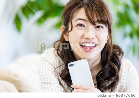 リビングのソファでスマホを見ながら微笑む女性 リビングのソファでスマホを見ながら微笑む女性 66377660
