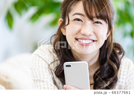 リビングのソファでスマホを見ながら微笑む女性 リビングのソファでスマホを見ながら微笑む女性 66377661