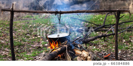 Cooking in old sooty cauldron on campfire 66384886