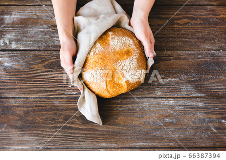 Hands holding a whole loaf of freshly baked bread with a golden crust. Homemade yeast-free pastries wooden background. 66387394