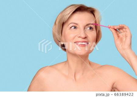 Middle aged woman correcting eyebrow shape using brush Middle aged woman correcting eyebrow shape using brush 66389422