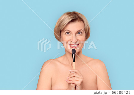 Mature aged woman holding makeup brush in hand Mature aged woman holding makeup brush in hand 66389423