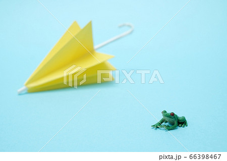 水色バックの折り紙の黄色い傘とカエルのフィギアの写真素材