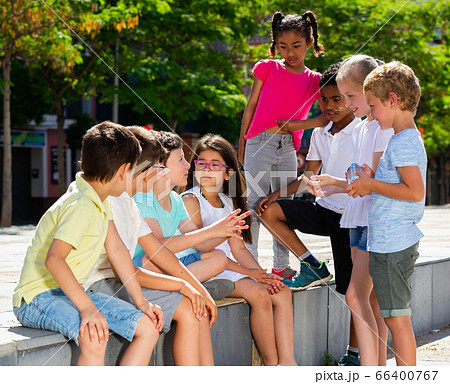 Group of cheerful children sitting on bench and sharing secrets 66400767