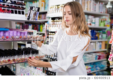 Young woman choosing lipsticks on stand in cosmetics store 66400913