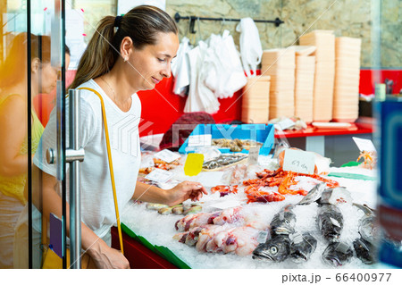 Focused woman searching for fresh seafood on icy showcase while shopping in fish store Focused woman searching for fresh seafood on icy showcase while shopping in fish store 66400977