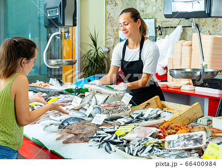 Confident worker offering fresh sea bass to woman Confident worker offering fresh sea bass to woman 66400984