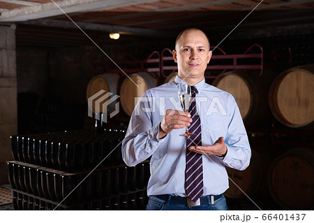 Confident winemaker offering glass of white sparkling wine for tasting in wine cellar Confident winemaker offering glass of white sparkling wine for tasting in wine cellar 66401437