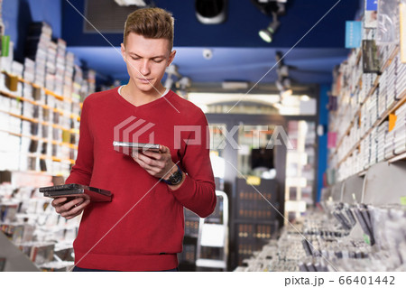 Guy looking CD and DVD in shop attentively reading contents Guy looking CD and DVD in shop attentively reading contents 66401442