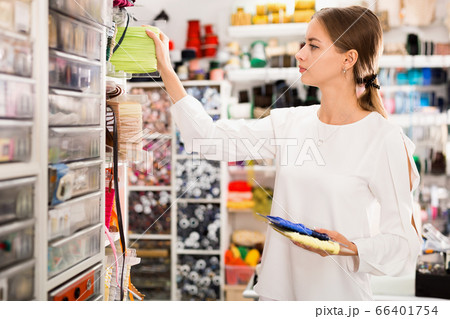 Interested young woman choosing colorful ribbons and braid for dressmaking in sewing supplies shop 66401754