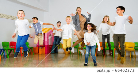 Positive female teacher and group of schoolkids jumping in classroom Positive female teacher and group of schoolkids jumping in classroom 66402373