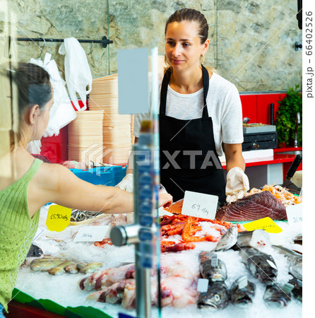 female fishmonger showing variety of fresh fish and seafoods female fishmonger showing variety of fresh fish and seafoods 66402526
