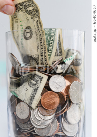 Close-up of fingers pulling one dollar bill from jar with American cents and banknotes 66404657