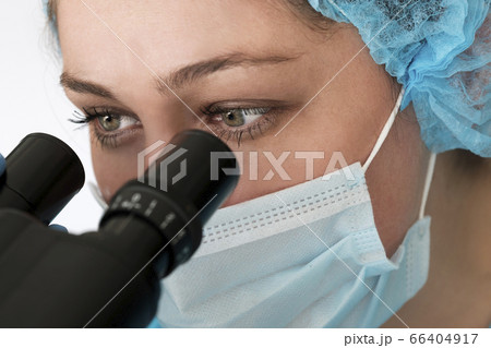 Laboratory technician in face mask looking through microscope 66404917