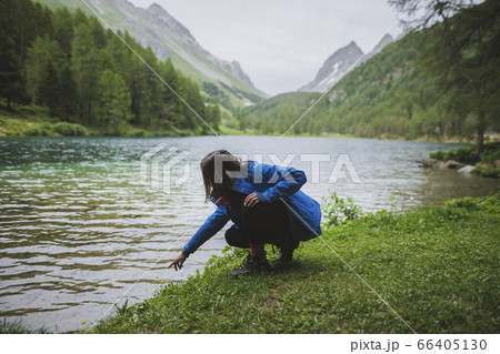 Switzerland, Bravuogn, Palpuognasee, Young woman crouching by Palpuognasee lake in Swiss Alps Switzerland, Bravuogn, Palpuognasee, Young woman crouching by Palpuognasee lake in Swiss Alps 66405130