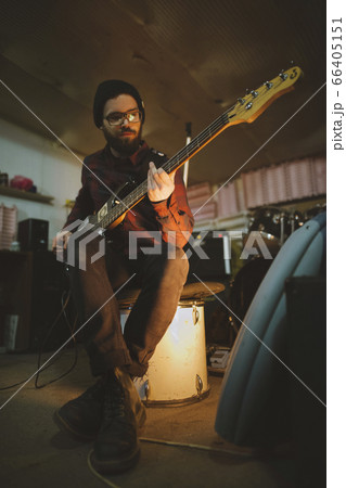 Young man playing bass guitar during rehearsal in garage 66405151