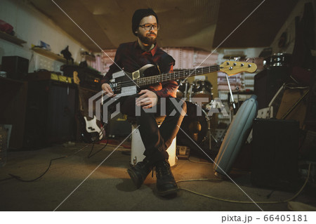 Young man playing bass guitar during rehearsal in garage 66405181