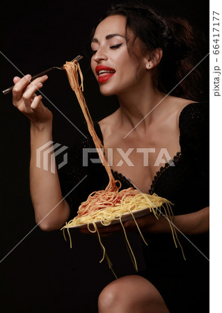 A beautiful girl eats with a fork spaghetti with red lips. 66417177