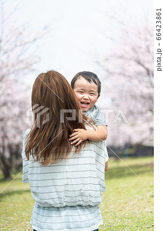 桜並木で男の子を抱っこする母親の後ろ姿の写真素材