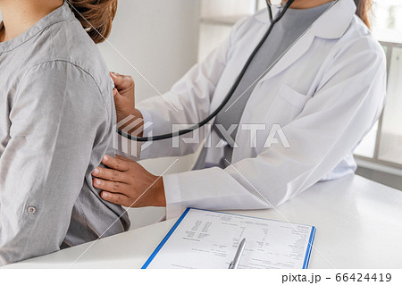 Doctor evaluates the patient with a stethoscope, blood pressure monitor and records the results 66424419