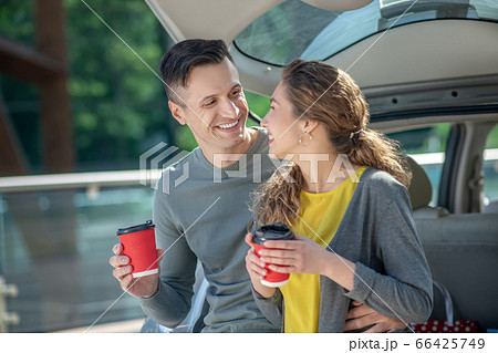 Loving man and woman drinking coffee near the car. Loving man and woman drinking coffee near the car. 66425749