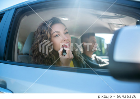 Beautiful woman painting lips in car looking in side mirror 66426326