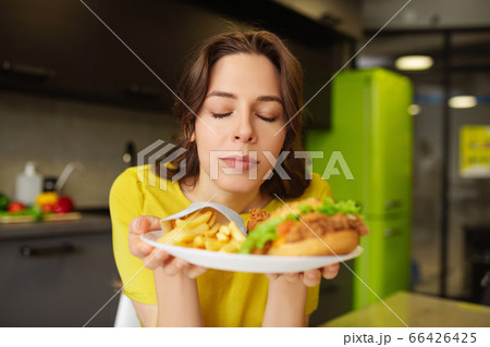 Happy woman with closed eyes with plate of fast food. Happy woman with closed eyes with plate of fast food. 66426425