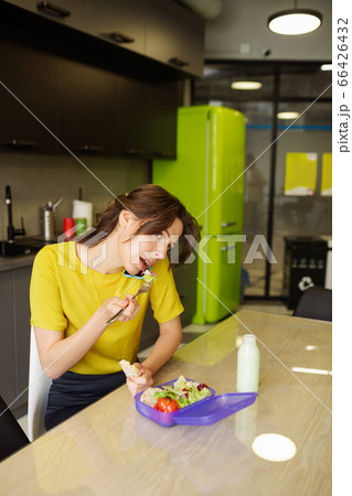 Young woman talking on smartphone and eating during lunch break Young woman talking on smartphone and eating during lunch break 66426432