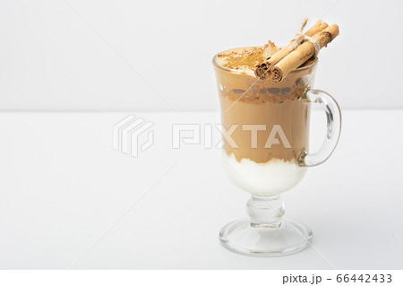 Dalgona Coffee Iced, a Korean fashionable whipped black instant coffee with milk, on a white background. On a glass of cinnamon sticks and chocolate chips. Copy space. Direct view. Dalgona Coffee Iced, a Korean fashionable whipped black instant coffee with milk, on a white background. On a glass of cinnamon sticks and chocolate chips. Copy space. Direct view. 66442433